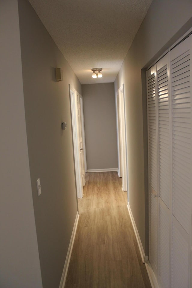 corridor with a textured ceiling and light wood-type flooring