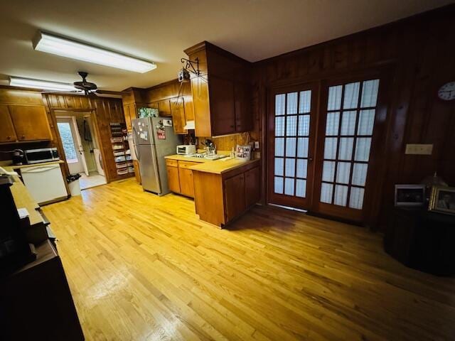 kitchen featuring kitchen peninsula, stainless steel appliances, ceiling fan, wooden walls, and light hardwood / wood-style floors