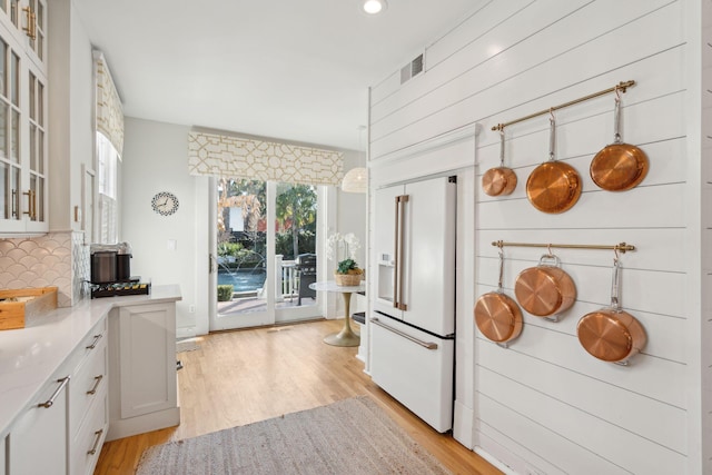 kitchen featuring white cabinetry, hanging light fixtures, backsplash, white built in refrigerator, and light wood-type flooring