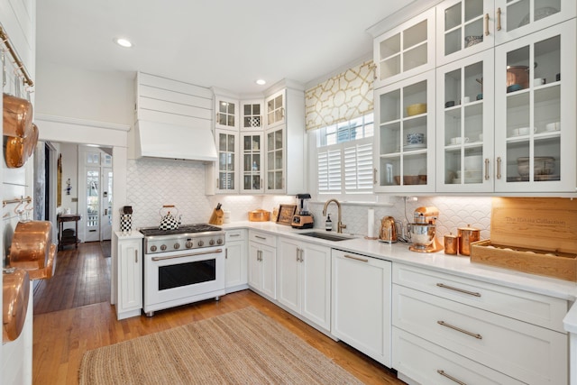 kitchen with premium range hood, white cabinetry, sink, high end white range oven, and light wood-type flooring