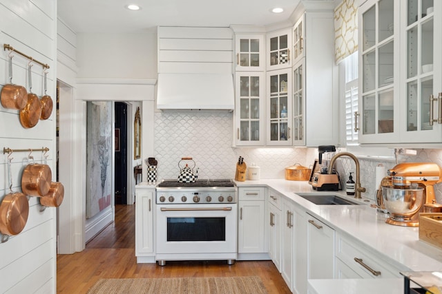 kitchen with sink, high quality range, light hardwood / wood-style floors, decorative backsplash, and white cabinets