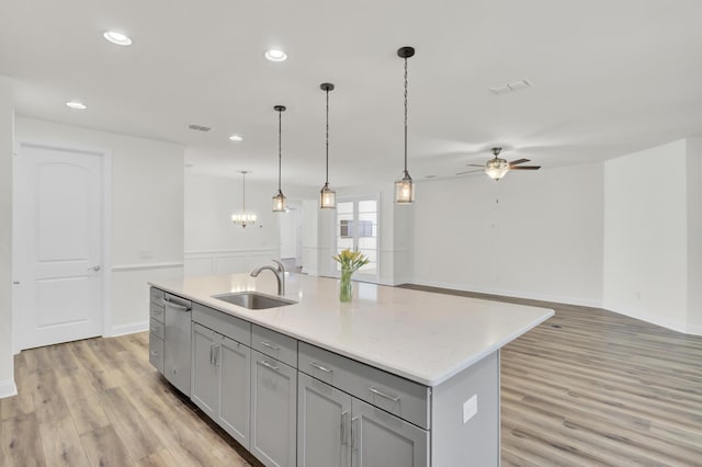 kitchen featuring an island with sink, gray cabinets, a sink, light wood-style flooring, and ceiling fan with notable chandelier