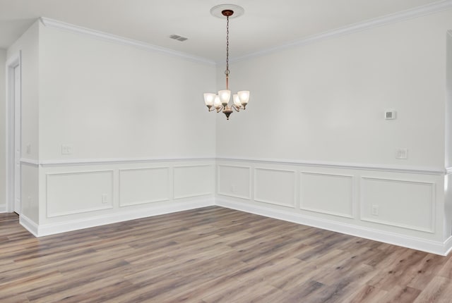spare room featuring wood finished floors, wainscoting, a chandelier, ornamental molding, and visible vents