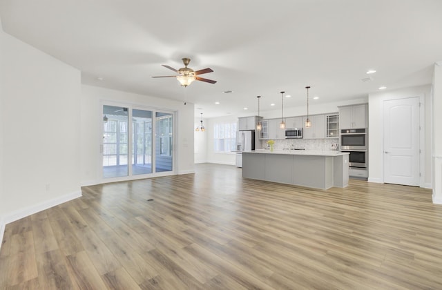 unfurnished living room with recessed lighting, light wood finished floors, a ceiling fan, and baseboards