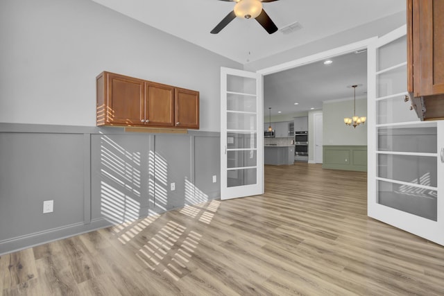 spare room with visible vents, a decorative wall, wainscoting, light wood-style flooring, and ceiling fan with notable chandelier