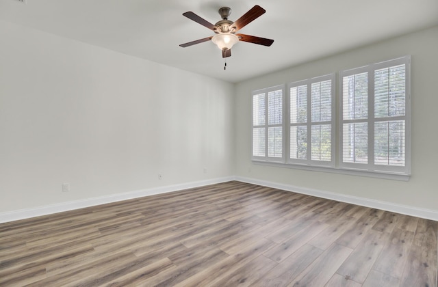 empty room with wood finished floors, a wealth of natural light, baseboards, and ceiling fan
