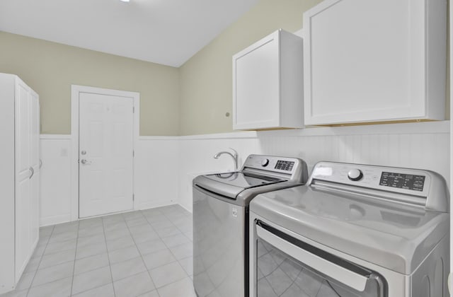 washroom with a wainscoted wall, washer and dryer, light tile patterned floors, and cabinet space