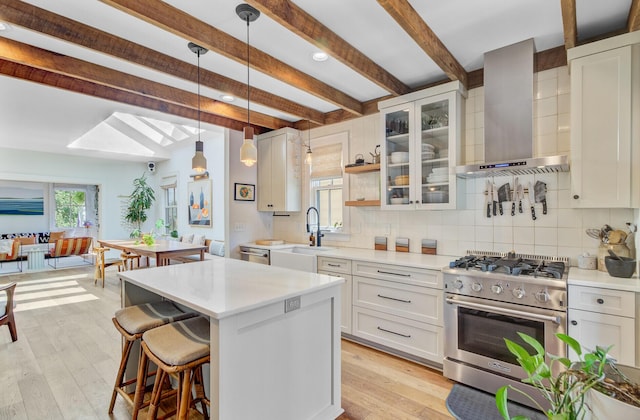 11 Francis St, Charleston, SC 29403 - kitchen featuring stainless steel appliances, wall chimney exhaust hood, beamed ceiling, light countertops, and decorative backsplash
