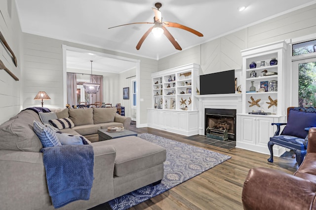 living room featuring dark hardwood / wood-style floors, ornamental molding, ceiling fan with notable chandelier, and wooden walls