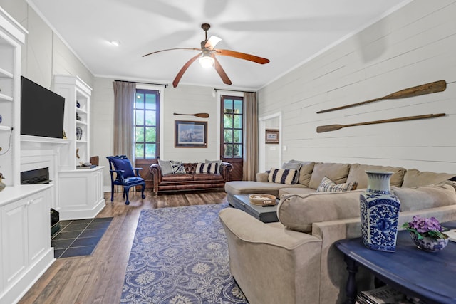 living room featuring wooden walls, ceiling fan, built in features, ornamental molding, and dark hardwood / wood-style flooring