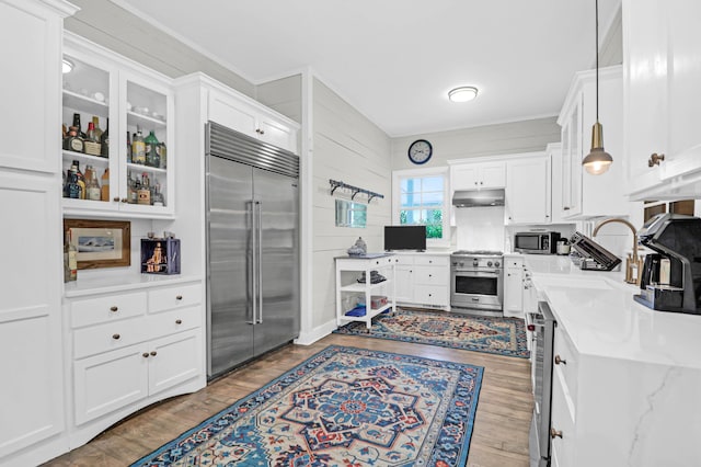 kitchen featuring decorative light fixtures, high end appliances, white cabinetry, and light stone counters