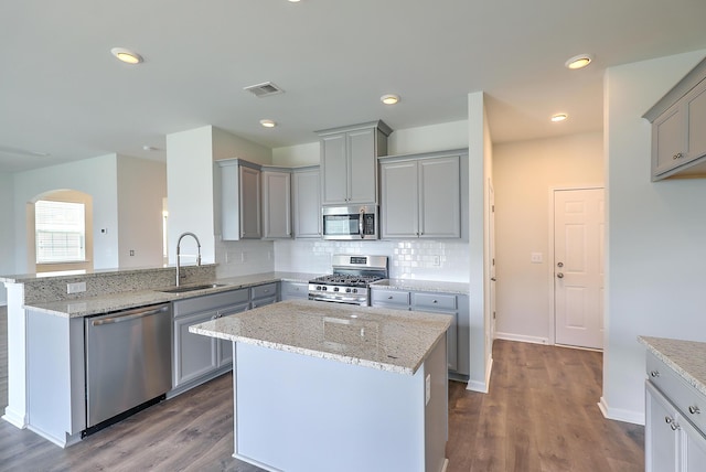 kitchen with light stone countertops, appliances with stainless steel finishes, a center island, and sink