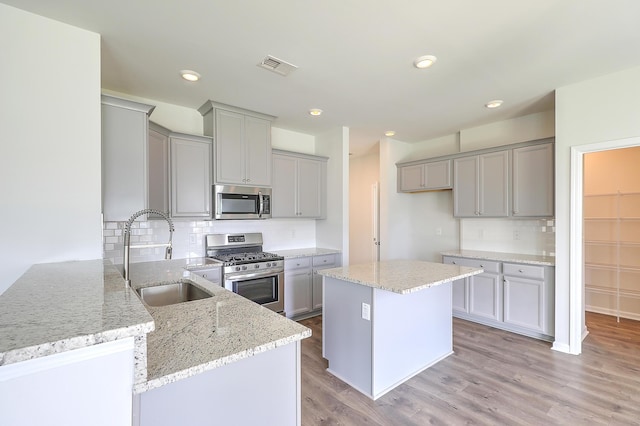 kitchen with backsplash, sink, light stone countertops, appliances with stainless steel finishes, and kitchen peninsula