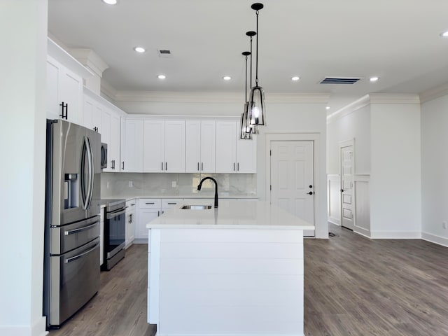 kitchen featuring appliances with stainless steel finishes, wood-type flooring, white cabinets, hanging light fixtures, and an island with sink