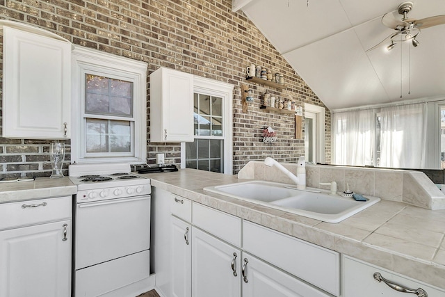 kitchen with sink, white electric stove, brick wall, and white cabinetry