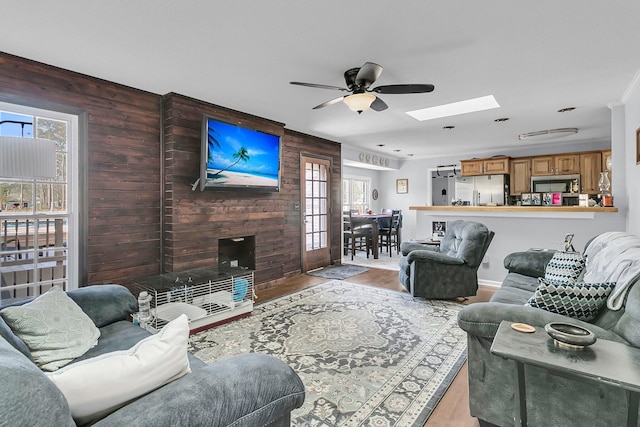 living room with light hardwood / wood-style floors, a fireplace, a skylight, ceiling fan, and wood walls