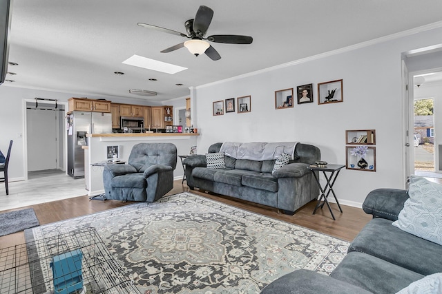 living room featuring ceiling fan, light hardwood / wood-style floors, a skylight, and ornamental molding