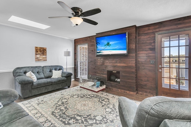 living room featuring a skylight, ceiling fan, wooden walls, and crown molding