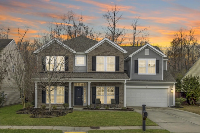 traditional-style house featuring covered porch, a shingled roof, concrete driveway, and a front yard