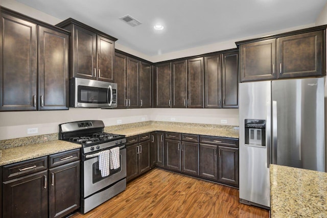 kitchen featuring dark wood-style flooring, visible vents, appliances with stainless steel finishes, dark brown cabinetry, and light stone countertops