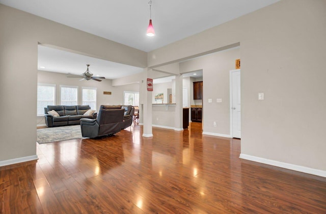 living area featuring a ceiling fan, baseboards, and dark wood-style flooring