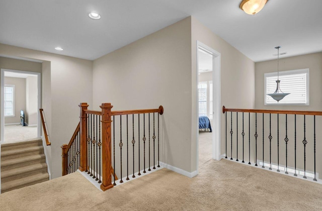 hallway featuring a healthy amount of sunlight, carpet flooring, and an upstairs landing