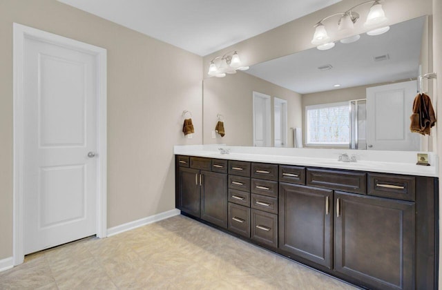 full bath with double vanity, visible vents, a shower with shower door, a sink, and baseboards