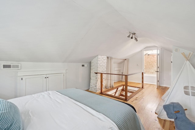 bedroom with light wood-type flooring, lofted ceiling, and connected bathroom