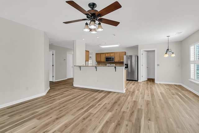 kitchen featuring light wood-style flooring, a peninsula, a kitchen breakfast bar, open floor plan, and appliances with stainless steel finishes