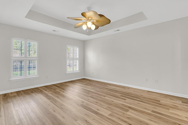 spare room with light wood-style floors, baseboards, visible vents, and a tray ceiling