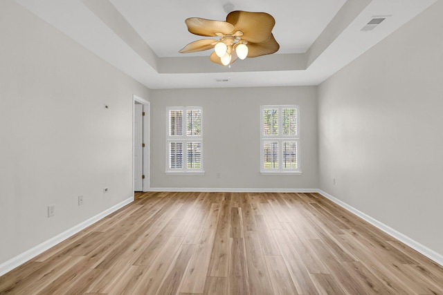 unfurnished room featuring light wood-style floors, baseboards, a tray ceiling, and a ceiling fan