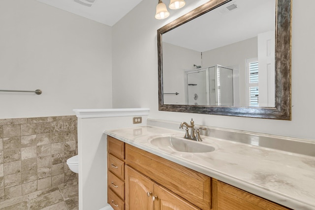 bathroom with visible vents, toilet, vanity, a shower stall, and tile walls