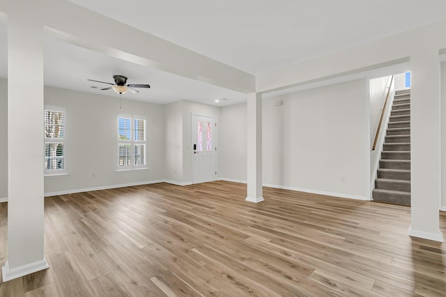 unfurnished living room with ceiling fan, stairway, light wood-style flooring, and baseboards