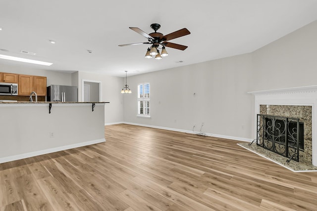 unfurnished living room featuring visible vents, light wood-style flooring, a ceiling fan, a high end fireplace, and baseboards