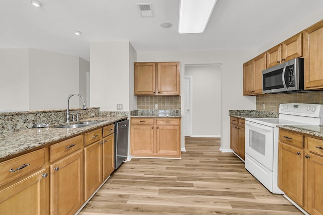 kitchen featuring light wood finished floors, stainless steel appliances, light stone counters, and a sink