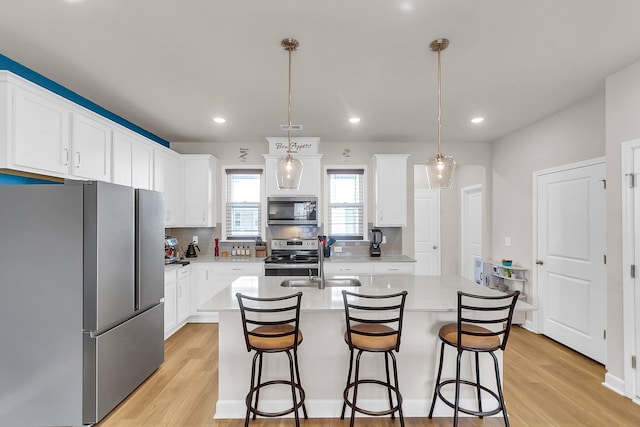 kitchen featuring stainless steel appliances, light hardwood / wood-style floors, a kitchen island with sink, white cabinetry, and decorative light fixtures