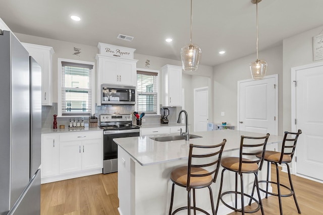 kitchen featuring white cabinetry, appliances with stainless steel finishes, hanging light fixtures, sink, and a healthy amount of sunlight