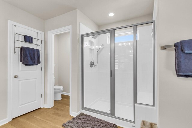 bathroom featuring wood-type flooring, toilet, and a shower with door