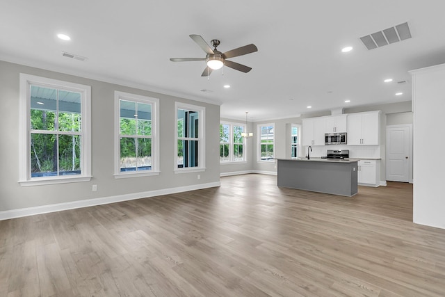 unfurnished living room featuring a sink, a ceiling fan, light wood finished floors, ornamental molding, and baseboards