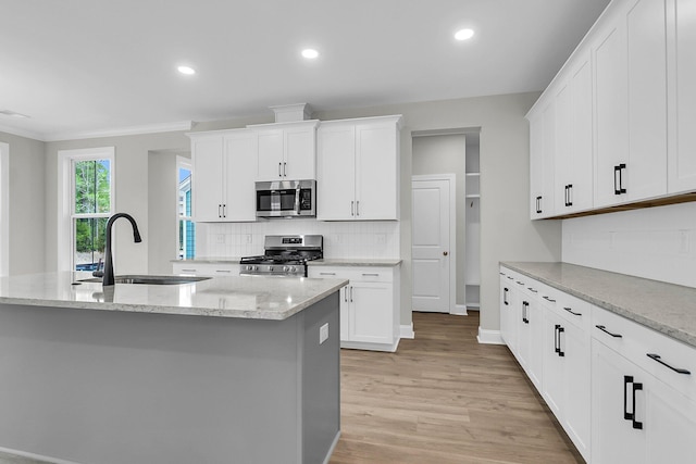 kitchen with stainless steel appliances, a sink, light wood finished floors, decorative backsplash, and white cabinets