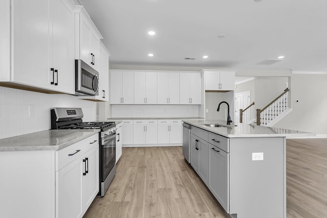 kitchen featuring appliances with stainless steel finishes, a sink, light wood finished floors, recessed lighting, and decorative backsplash