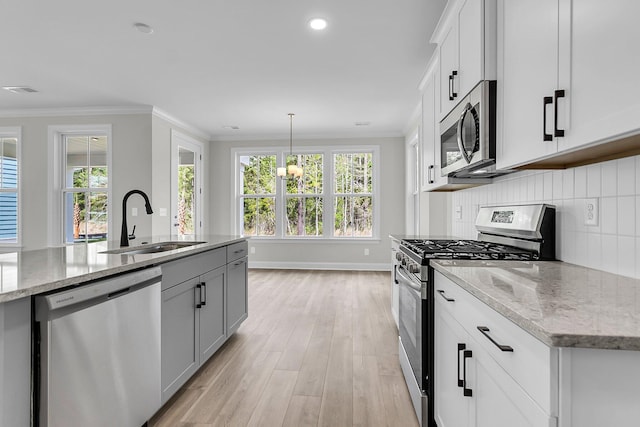 kitchen featuring stainless steel appliances, a sink, light wood finished floors, crown molding, and decorative backsplash