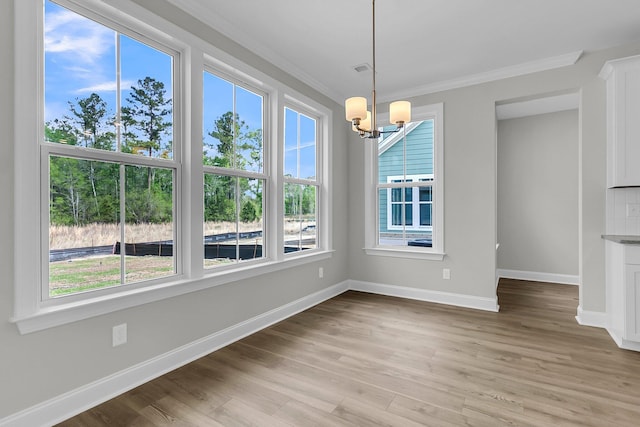 unfurnished dining area with a chandelier, crown molding, baseboards, and light wood finished floors