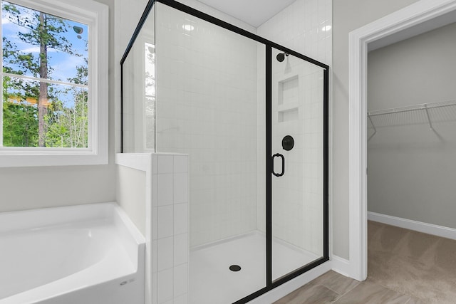 bathroom with a stall shower, a spacious closet, a garden tub, and baseboards