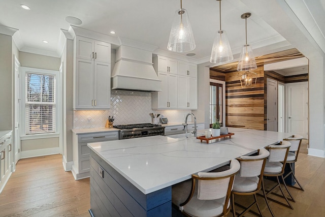 kitchen with a center island with sink, premium range hood, crown molding, range, and light wood-type flooring