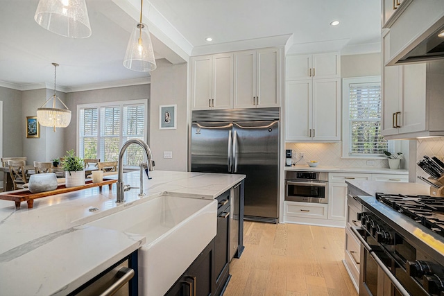 kitchen featuring crown molding, wall chimney range hood, appliances with stainless steel finishes, and a sink