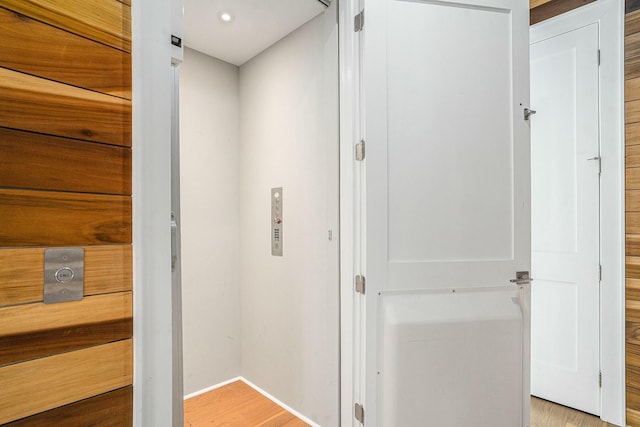 hall featuring baseboards, elevator, and light wood-style flooring