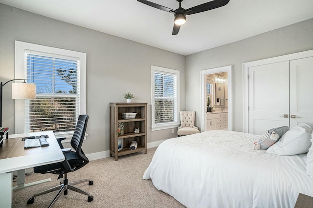 bedroom featuring baseboards, ensuite bath, ceiling fan, a closet, and light colored carpet