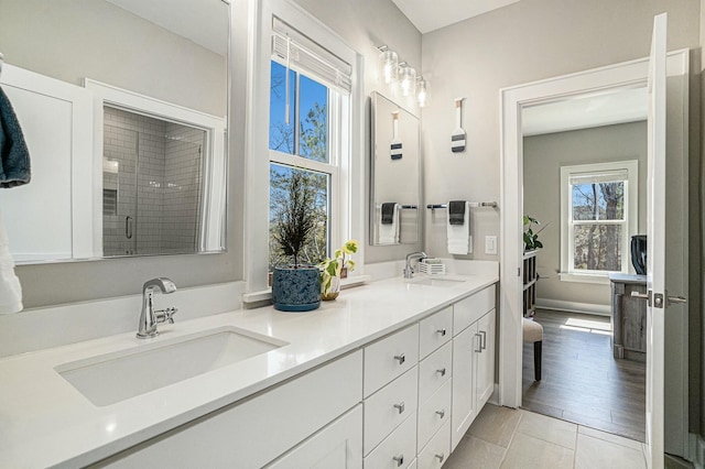 full bathroom featuring a sink, baseboards, a shower stall, and double vanity