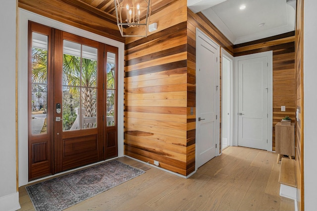 entryway featuring wooden walls, a notable chandelier, and light wood finished floors